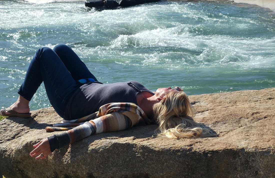 Misti Spencer resting on a sunlit rock beside rushing spring water